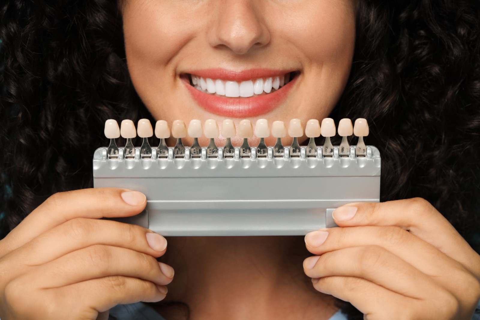 Shade guide held against a patient’s smile